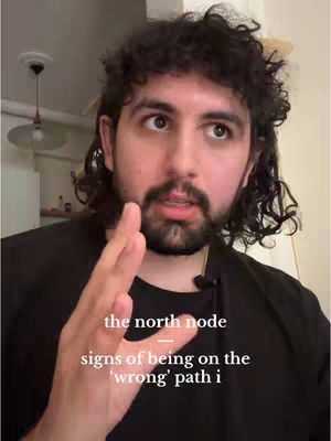 A man with dark curly hair and a beard is the focus, set against a blurred indoor background. He's wearing a black shirt and looking upwards with an open expression, his hand raised partially in front of his face. Overlayed on the image are the words 'the north node', 'signs of being on the', and 'wrong' path i'.