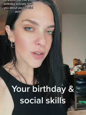 A medium close-up shot features a light-skinned woman with dark hair, wearing a black top, looking slightly to the right in front of an out-of-focus indoor background.
