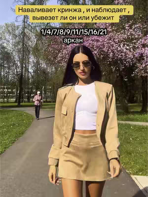 A woman in sunglasses and a tan outfit stands on a path. A text overlay in a yellow box is at the top, and a figure walks in the background.