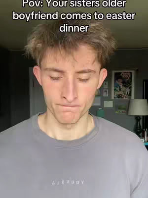 A young man with light brown hair looks down, seemingly sad or embarrassed. Above him, capitalized text reads 'POV: Your sisters older boyfriend comes to east dinner.' He wears a gray sweatshirt. The background is a living space with framed art and a lamp.