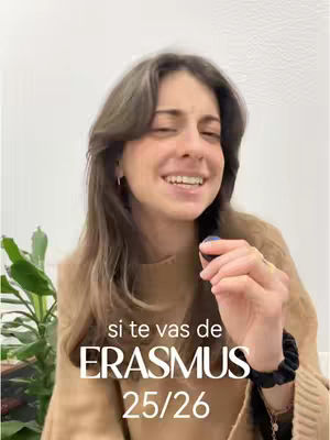 A woman with long brown hair smiles, holding a dark object, likely a phone. Text overlays read "si te vas de" and "ERASMUS 25/26". The background appears to be a plain white wall with some greenery to the left.