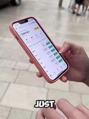 The cover image shows a close-up of a person's hand holding a pink iPhone. The phone screen displays a trading app interface with numeric data and green highlighted entries. The bottom of the image shows overlaid text in impact font: 'JUST'. The background is blurred, suggesting an outdoor setting.