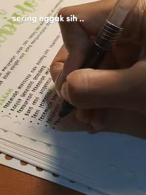 Close-up shot of a hand writing on a notebook. The hand holds a black pen and is actively writing on a page filled with handwritten notes and bullet points. The lighting is soft, with a focus the notebook.