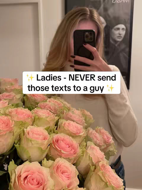 A woman is taking a selfie in front of a mirror, using a smartphone to obscure her face. She's holding a large bouquet of pink and peach roses in her arms. A framed portrait hangs behind her. A white text box with sparkles is overlayed on the image.