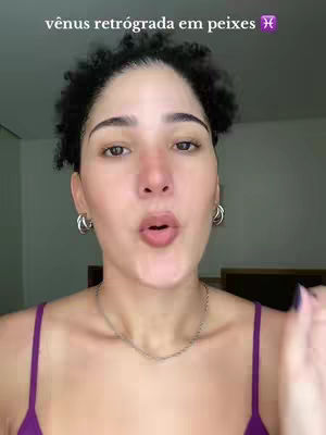 The cover image showcases a close-up of a woman's face. She has short, dark, curly hair and is wearing hoop earrings and a purple top. A silver necklace rests on her neck. The background appears to be a neutral-toned wall. Above her head, the text "vênus retrógrada em peixes" is visible.