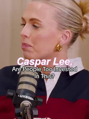 A woman is centered in a medium shot, her head and upper body visible as she looks slightly off-camera to the left. She has light skin, blonde hair pulled back in a low bun, and is wearing gold hoop earrings. A microphone with the 'LUXEGEN' logo is positioned in front of her. Overlayed in the image is text: 'Caspar Lee, Are People Too Invested In This?' The background appears to be a neutral color, with some lighting. The woman is wearing a dark shirt with a red and white collar.