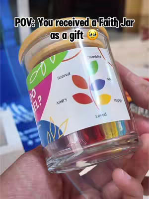 The image shows a hand holding a jar. The jar has a wooden lid and a label with the words "Scared," "Angry," "Sad," "Happy," and "Loved" written around colorful leaves. The text "POV: You received a Faith Jar as a gift" is at the top.