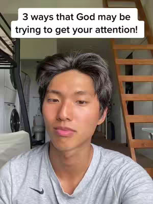 A young Asian man in a grey t-shirt with a black Nike logo is the central figure, positioned from the chest up. Above him is a white rectangular box with black text, which serves as the main hook of the image. The background is blurred, consisting of domestic elements that could be part of a home, including a staircase and parts of furniture. The lighting is natural and the overall composition gives a casual, everyday ambiance.
