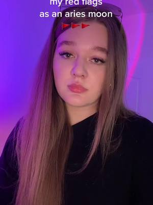 A young woman with long, light brown hair is centered in a medium shot. She has a fair complexion, full lips, and is looking directly at the camera with a slightly serious expression. Her eyes are visible and her brow is slightly furrowed, suggesting contemplation or a slight concern. Over her head is text with three red flag emojis. The background is a gradient of purple hues.