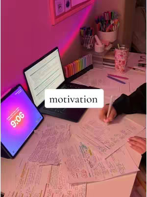 A workspace is shown with a laptop, tablet displaying 9:06, textbooks, and stationery. A hand is writing on a paper. The wall is pink, and the scene is lit with a pink and purple glow, with the added text overlayed with the word motivation.