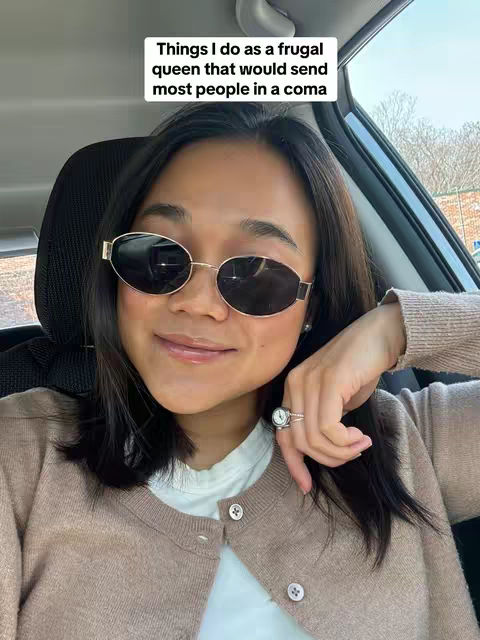A selfie taken from inside a car shows a woman with dark hair, wearing sunglasses and a light-brown cardigan. She is smiling slightly, and her right hand rests near her face, displaying a ring. A text overlay at the top reads 'Things I do as a frugal queen that would send most people in a coma.'
