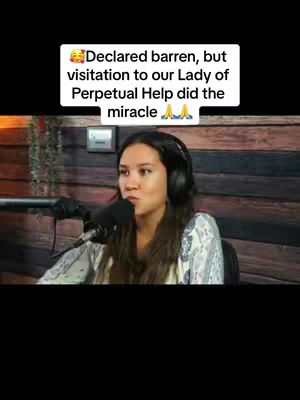 A woman with long, dark hair wearing a headset and a light-colored patterned top speaks into a microphone. She is in a setting with a wooden background and a small light fixture. An overlaid text box at the top of the image has the message, "Declared barren, but visitation to our Lady of Perpetual Help did the miracle."