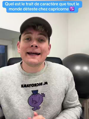 A man in a gray Mr. Men themed sweatshirt speaks directly to the camera, with a blue speech bubble above his head containing text about Capricorn traits. To his right, a large black exercise ball is visible.