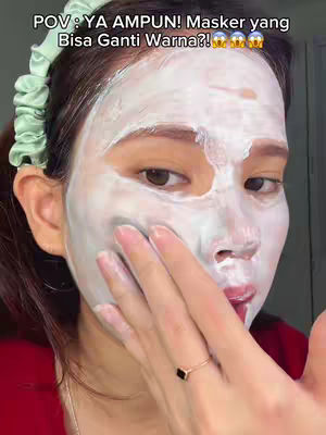A close-up shot features a woman with a white face mask, touching her face. She is wearing a red top, with a green scrunchie holding her hair back. Text overlay in the top left corner.
