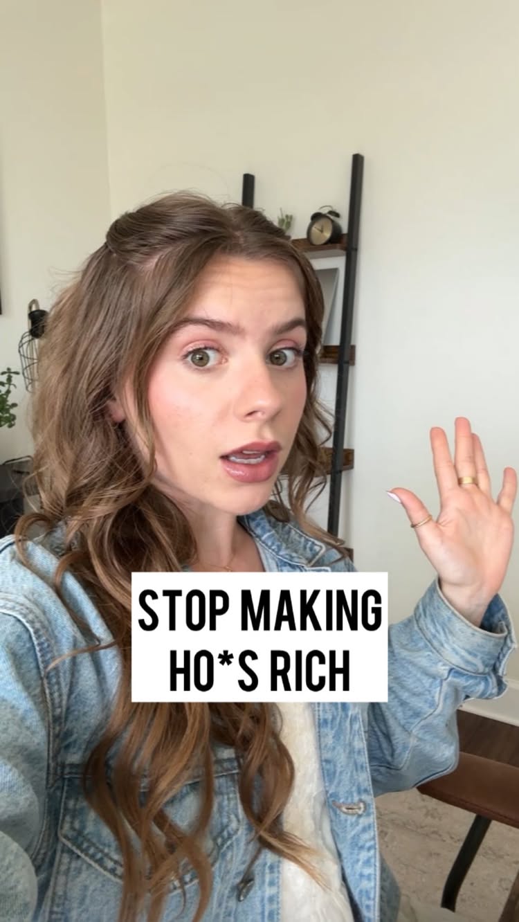 A woman with long, wavy brown hair and a denim jacket is looking at the camera with a slightly surprised expression, her right hand raised with her palm facing forward. She is standing in front of a light-colored wall with a shelf and clock visible in the background. A white box with black text overlays the image, reading 'STOP MAKING HO*S RICH'.