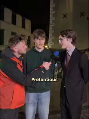 Three men are standing on a street at night, with a dark background of buildings and a street light illuminating the scene. One man is holding a microphone and interviewing subjects, and the text overlay appears in the middle of the scene.