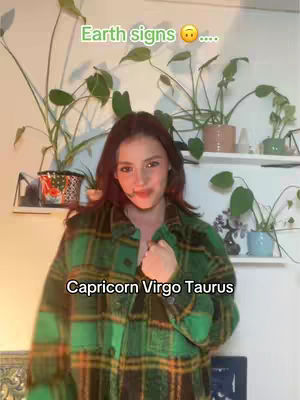 A woman with long brown hair wearing a green and black plaid shirt stands in front of a white wall with plants on shelves behind her. Text overlays appear on the image.
