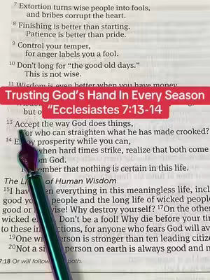 The image shows an open book with text on its pages. A colorful pen is vertically positioned on the page, with its tip pointing to the text. A red horizontal bar with white text reading "Trusting God's Hand In Every Season" and "Ecclesiastes 7:13-14" is placed over the text.