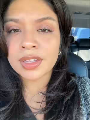 A close-up of a woman's face in a car, looking at the camera with a serious expression. The lighting appears to be natural, and the background is blurred, focusing primarily on her face.
