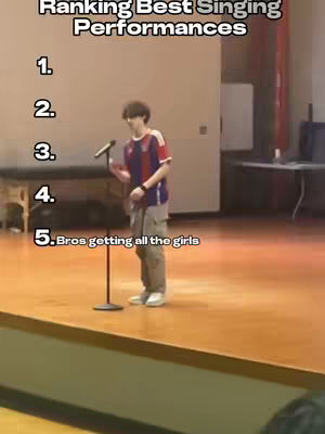 A person in civilian clothes with a shirt that has red, blue, and white standing on a stage in front of a microphone.