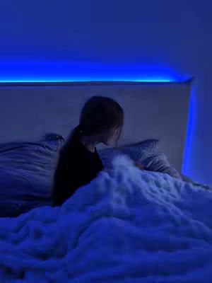 The cover image shows a person lying in bed, their back towards the camera. The scene is dimly lit with a blue hue, suggesting a nighttime or indoor setting. A blanket covers the person up to their shoulders, and a portion of a headboard and pillows are visible. The overall composition is intimate and captures a moment of relaxation.