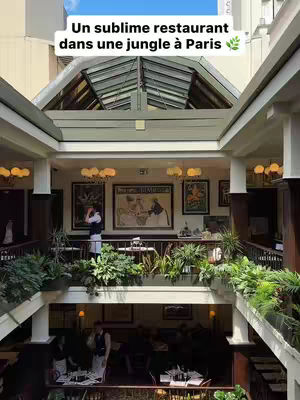 The cover image shows a multi-story building with a glass roof and balconies. There are multiple floors with tables and chairs, and people are sitting at the tables. There is a lot of greenery surrounding the building. A text overlay provides a hook for the video.