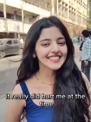 A young woman with long, dark hair smiles broadly, set against an out-of-focus urban background. The text overlayed says 'it really did hurt me at the time'.