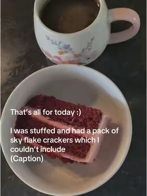 A photo featuring a slice of red velvet cake on a white plate, with a cup of coffee or tea in a floral-patterned mug in the background. Text overlays provide context and information. The overall composition is simple and suggests a casual setting.