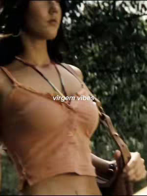 The cover image features a medium shot of a woman walking forward while looking away from the camera, suggesting movement. She is wearing a peach-colored top with spaghetti straps, and a multi-strand necklace. The background appears blurred, with green foliage, indicating an outdoor setting. Text labeled 'Virgem vibes' is overlayed across the image.