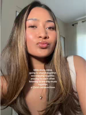 A selfie-style shot of a woman with long, highlighted hair and a neutral expression, slightly puckering her lips. She wears a white top and a delicate necklace. Text overlays with various aspects of a Christ-centered love.