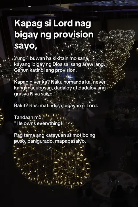 The image presents a dimly lit interior, likely a venue, with a focus on decorative lighting fixtures. These fixtures consist of numerous spherical or orb-like structures, each dotted with small, bright lights, suggesting string lights or similar illumination. The overall effect is one of subtle elegance and warmth, creating a visually engaging pattern against the darker background. Text in Tagalog is overlaid on the image, presenting motivational or religious content. The composition is simple, drawing attention to the text and the overall ambiance.