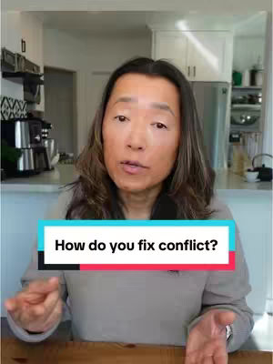 A woman with long brown hair sits in front of a kitchen background. She is looking toward the camera and talking. A text overlay box appears in front of her.