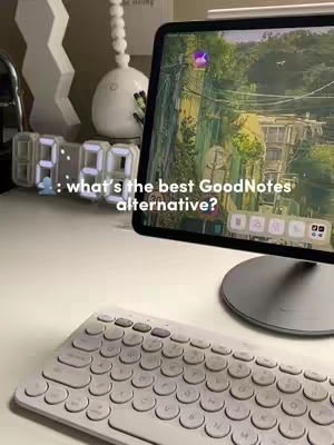 A well-lit workspace with a white desk featuring a tablet displaying a nature scene, a white keyboard, a digital clock showing time, and decorative items. The overall composition suggests a study or work environment.