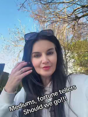 A selfie-style shot features a woman in front of a backdrop of trees and a bright blue sky. Sunglasses are perched on her dark hair and she's wearing a white top. The text overlay is at the bottom, suggesting the video's focus on mediums and fortune tellers.