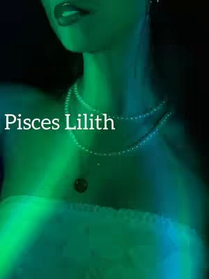 A person's face and upper chest are seen in a close-up shot. The skin has a green hue with the lights in the background, giving it an ethereal look. The person wears a pearl necklace and has their mouth slightly open with red lipstick, and text overlayed in white 'Pisces Lilith'.