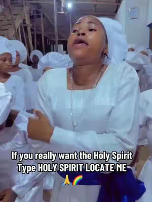 A woman in a white religious garment with a white head covering, standing in a room with other people dressed similarly. Text overlay at the bottom.