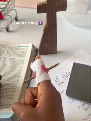 A close-up shot of a bible open to a passage, a wooden cross, a hand with a finger wrapped in a bandage with a pencil going through it. The text overlay reads "Good Friday". There are elements like a notepad and what seems to be a shopping cart in the background.