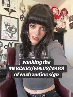 A person with dark hair and bangs sits in a burgundy chair. A text overlay reads "ranking the MERCURY/VENUS/MARS of each zodiac sign". The background includes a variety of framed pictures and decor.