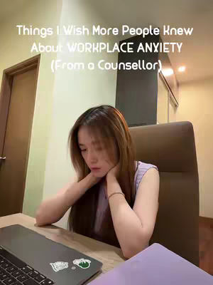 The cover image features a woman sitting at a desk with a laptop. The woman is the primary focus, with her head resting on her hands and looking down towards the laptop. The background includes a door, wall, and chair. The text overlay at the top reads, "Things I Wish More People Knew About WORKPLACE ANXIETY (From a Counsellor)"