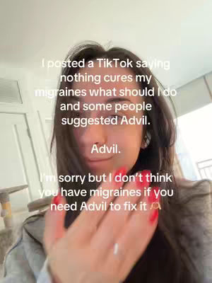 A selfie-style video shot with the creator taking up most of the frame. The background is a lightly blurred indoor setting, likely a home. The creator is a young woman with dark hair, looking directly at the camera. She has a slightly raised left hand with red nail polish, and text overlays the image, discussing migraines and the effectiveness of Advil.