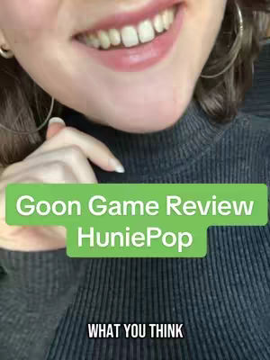A close-up shot features a smiling person's mouth and lower face, with a green rectangle overlaying text. The person has light skin, visible teeth, and some lip color. The background includes a dark gray, textured turtleneck. The text overlay reads 'Goon Game Review HuniePop', followed by the text 'WHAT YOU THINK' in white capital letters.