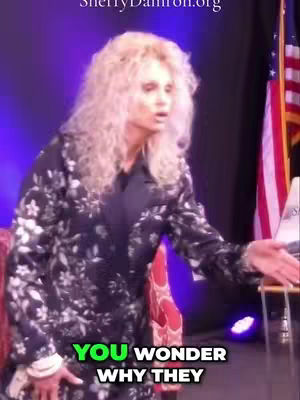 A woman with curly blonde hair, wearing a dark floral patterned jacket, stands in front of a blurred, purple-lit background, with a red-and-white striped item on her left, an American flag on her right, and a chair to her right. The hook features green text over the image, and Sherry Damron's website URL is at the top.