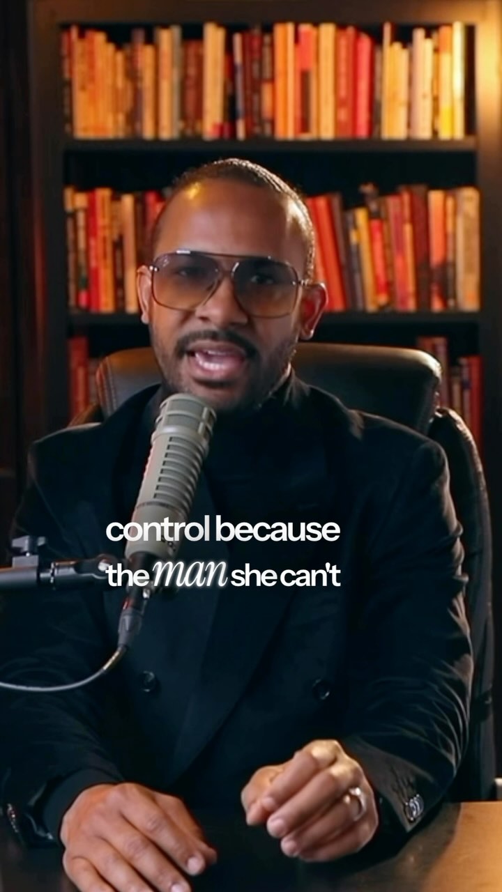 A man in a black suit and sunglasses speaks earnestly into a microphone against a backdrop of books. Text overlay is present.
