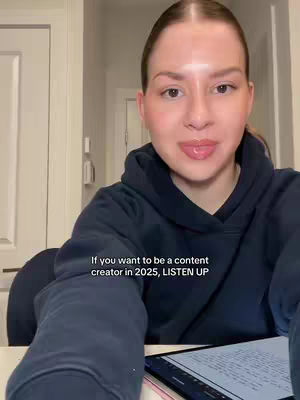A woman wearing a blue hoodie looks directly at the camera. Text overlayed at the bottom reads, 'If you want to be a content creator in 2025, LISTEN UP.' A tablet partially visible in the foreground displays text.
