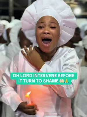 A woman in a white head covering and robe cries with her mouth open in a scream while holding a candle. Other figures in white clothing are blurred in the background.