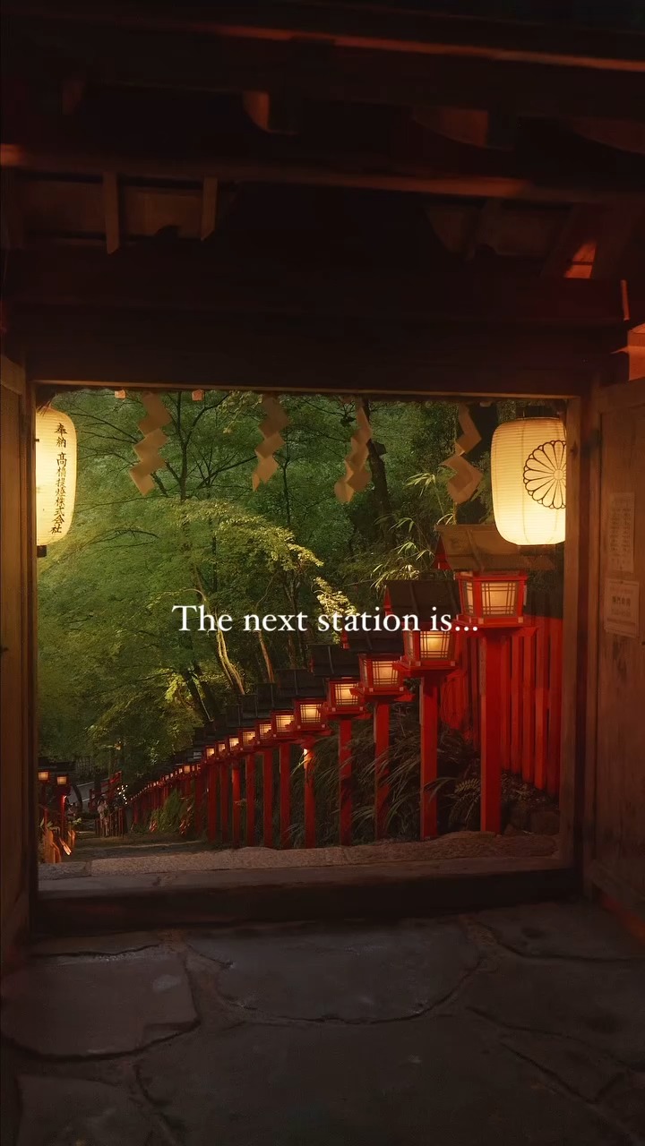 The image captures a scenic view of a path framed by a traditional wooden structure, leading the eye towards a lush green landscape. Along the path, a series of red lanterns are illuminated, guiding the viewer's gaze into the distance. The text overlay 'The next station is...' adds a sense of anticipation.