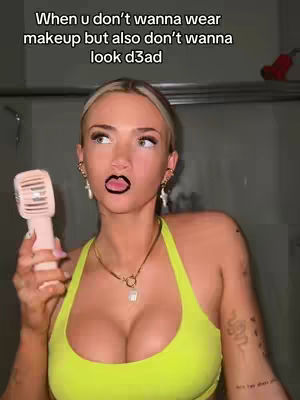 A woman in a tank top is holding a small fan in front of her face in what looks to be a bathroom. Above her head is the text, "When u don't wanna wear makeup but also don't wanna look d3ad." She has a dark lip stain and various jewelry.