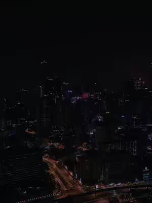 Night cityscape with buildings and roads illuminated by lights under a dark sky.