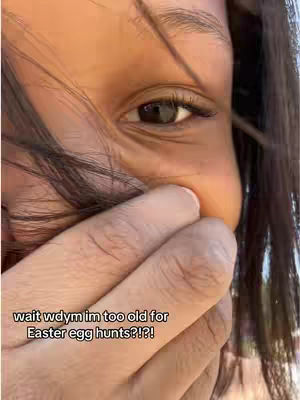 A close-up shot of a person's face, focusing on their right eye and hand covering their mouth. The person appears to be concealing laughter or surprise. Text overlayed on the image reads "wait wdym im too old for Easter egg hunts?!?!"