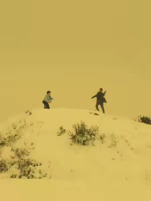 Two figures are engaged in a playful snowball fight on a snow-covered hill, set against a soft, golden-yellow sky that suggests either a sunrise or sunset. The snow is the primary element, textured with subtle variations. The overall composition is balanced, with the figures positioned to create a sense of action the focus of the image.